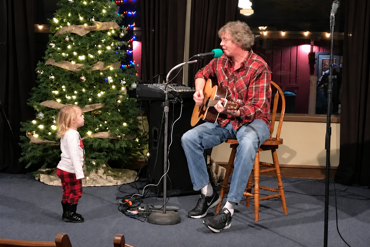 Guitar player performing beside a Christmas tree in the Fireside Room